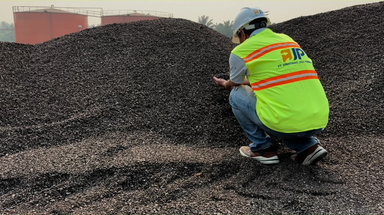 A person wearing an AJP vest examining palm kernel shells at a stockpile