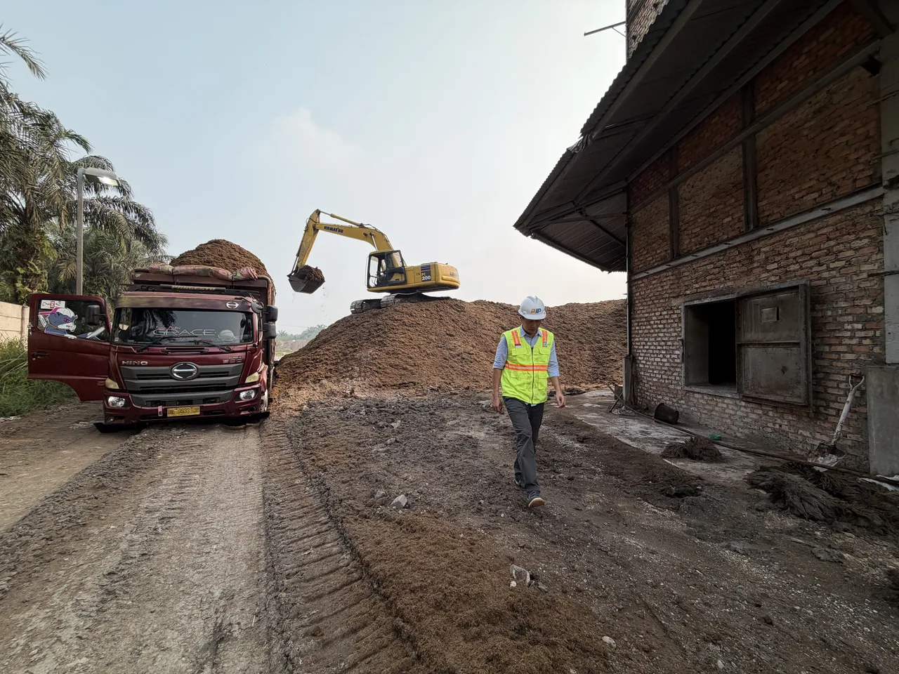 A truck beside a fibre stockpile, with an excavator and an AJP representative nearby