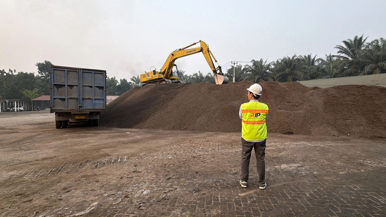 AJP representative beside a palm kernel shell stockpile, with an excavator and truck.